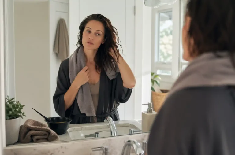 Femme aux cheveux humides essorés prête à appliquer une coloration dans sa salle de bain
